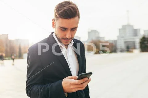Millennial businessman looks into the screen of his mobile phone. Close-up po Stock Photos
