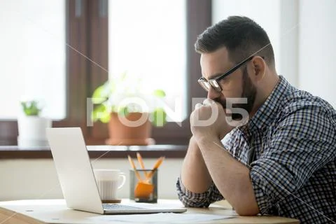 Millennial casual businessman thinking and looking at laptop in Stock Photos