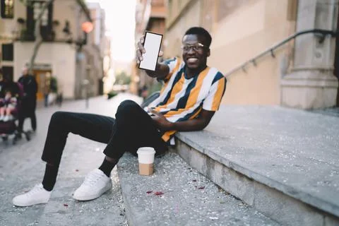 Millennial dark skinned hipster guy holding blank mobile phone with mockup for Stock Photos