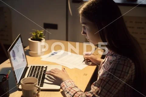 Millennial female employer typing on laptop and signing on docum Stock Photos