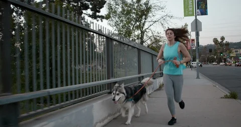 Millennial Female in Teal Running with Husky Dog Using Smart Watch Stock Footage