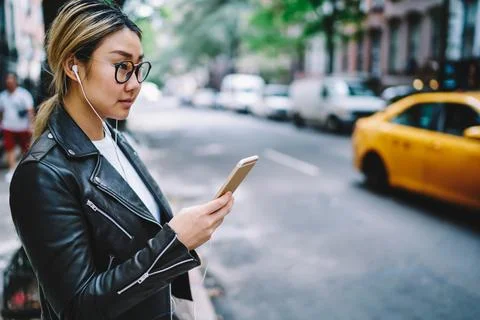 Millennial female using smartphone application for listening music song in city Stock Photos