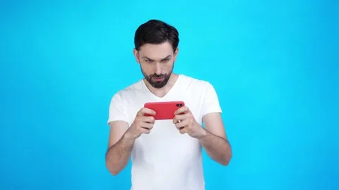 Millennial guy play smart phone fists up win isolated blue color background Video stock 165403191