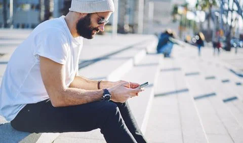 Millennial hipster guy in sunglasses browsing website via mobile technology Stock Photos
