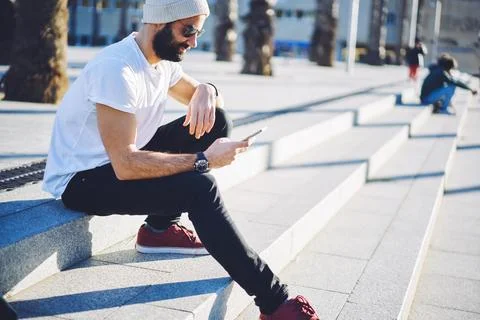Millennial hipster guy in sunglasses browsing website via mobile technology Stock Photos