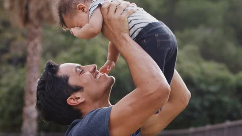Millennial Hispanic man lifting his baby son in the air in the park, close up Stock Footage 106688157