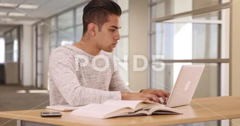 Millennial Hispanic university student in campus library with laptop and Stock Photos