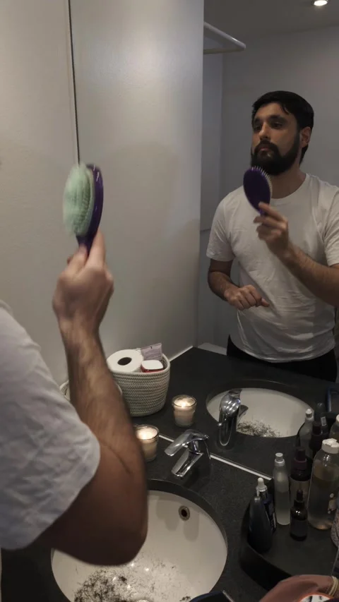 Millennial man brushing thick beard in bathroom mirror before trimming Video stock 335637000