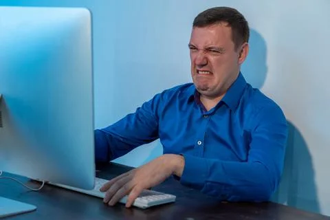 Millennial man looking disgusted in front of his computer in office. Confused Stock Photos