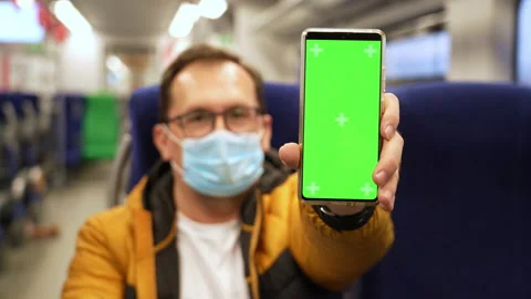 Millennial man in mask rides on train and presents phone with chromakey to Stock Footage 168244162