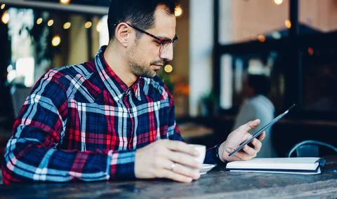 Millennial man in spectacles using digital tablet for browsing text on website Stock Photos