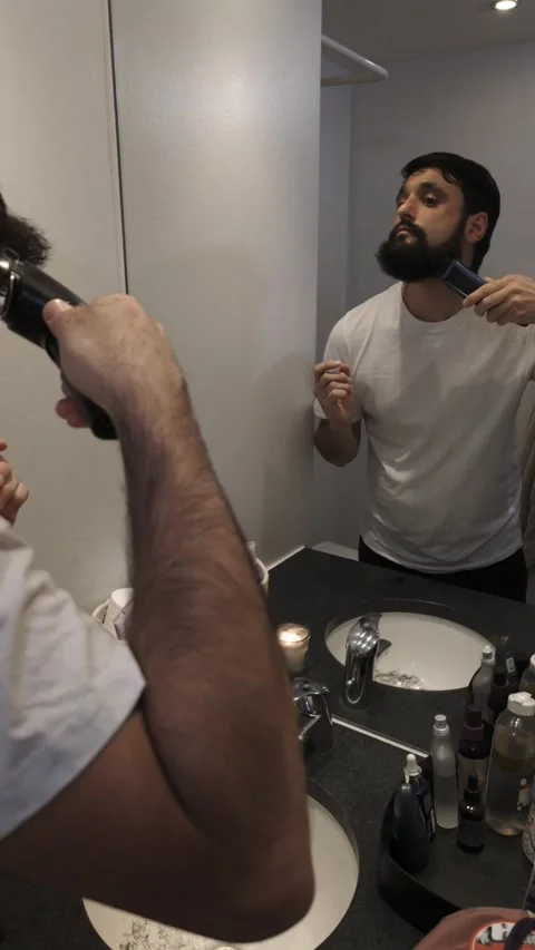 Millennial man trimming beard with electric shaver in stylish bathroom Video stock 335637295