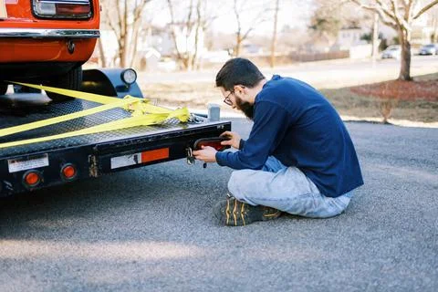 Millennial mechanic in driveway repairing tail light of a car hauler Stock Photos