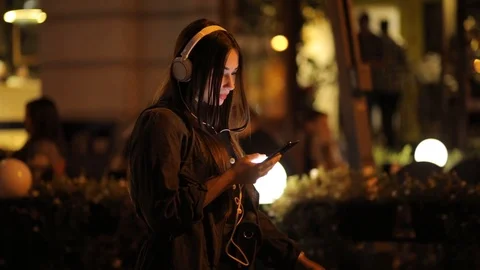 Millennial using smartphone walking in the night city. Stylish woman texting and Stock Footage 120084133