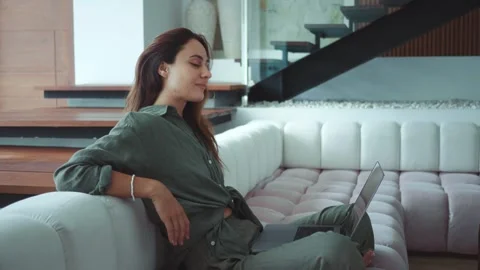Millennial woman seated on sofa using laptop for remote work modern technology Stock Footage 312509077