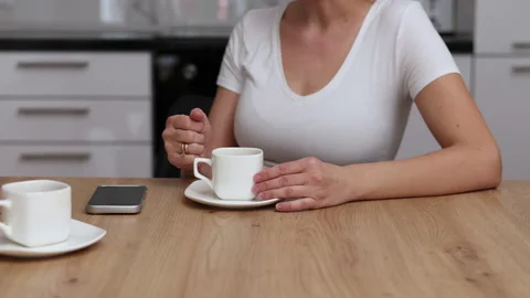 Millennial woman sitting in kitchen drinking coffee using smartphone Stock Footage 239302995