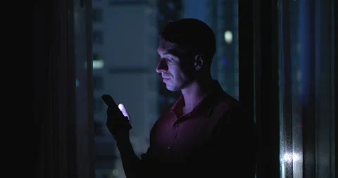 Millennials use mobile phone while standing by window at night. Man is in his Stock Footage 263407368
