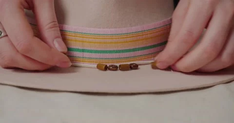 Milliner puts brown beads in row near ribbon on felt hat Stock Footage 207454094