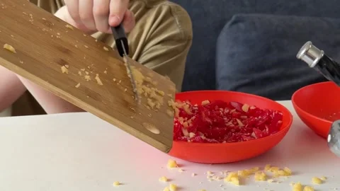Minced garlic being mixed with diced tomatoes in a red bowl, child’s hands only, Stock Footage 337414511