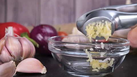 Minced garlic using a crusher or press in glass bowl Stock Footage 232415336