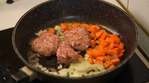 Minced meat patties cooking in pan with chopped carrots and onions. Stock Footage 342955209