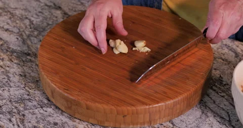Mincing garlic cloves on bamboo cutting board with chef's knife. Video stock 138468179