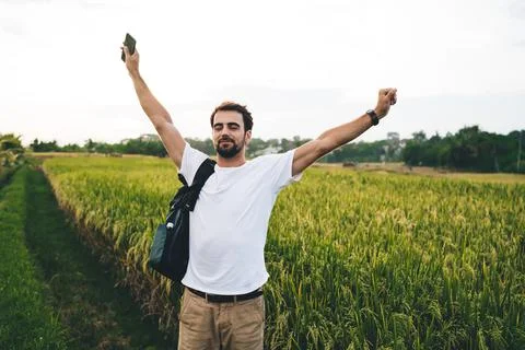 Mindful backpacker with raised arms on path against agricultural field Stock Photos