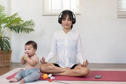Mindful mother meditating with headphones while her baby plays nearby, promoting Stock Photos