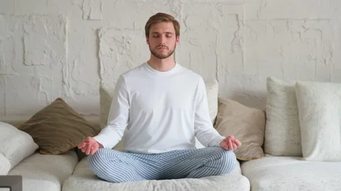 Mindfulness, young man sits on a sofa in the living room and meditates, a calm Stock Footage 154230827