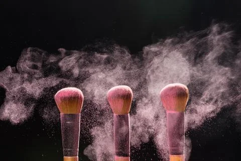 Mineral make up and objects concept - Three make up brushers in pink dust over Stock Photos
