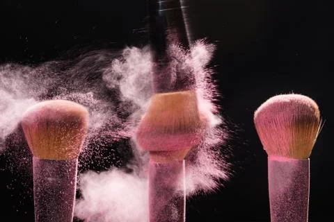 Mineral make up and objects concept - Three make up brushers in pink dust over Foto stock