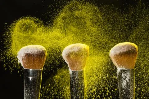 Mineral make up and objects concept - Three make up brushers in yellow dust over Foto stock