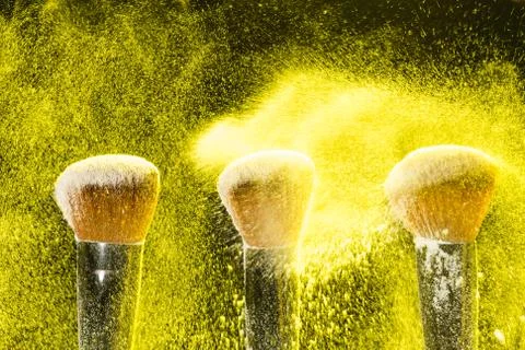 Mineral make up and objects concept - Three make up brushers in yellow dust over Stock Photos