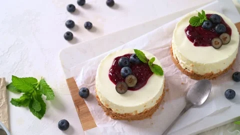 Mini cheesecakes topped with blueberry jam fresh berries and mint leaves on a wh Stock Footage 341710300