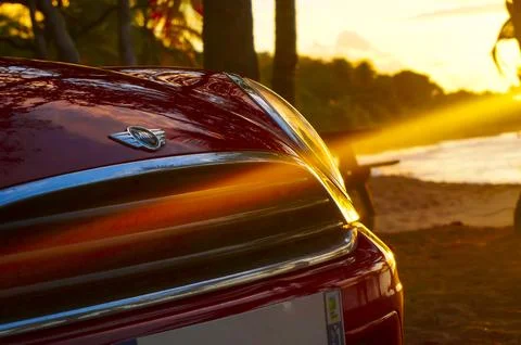 Mini Cooper parked on a sunset beach with sun rays Stock Photos