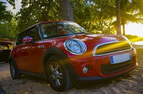 Mini Cooper parked on a sunset beach with sun rays Stock Photos