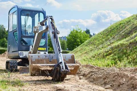 A mini crawler excavator digs the ground on a sunny day Stock Photos