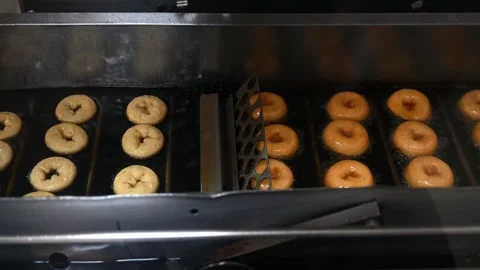 Mini donuts are flipped and fried in oil on an automated conveyor line. The Stock Footage 244683642