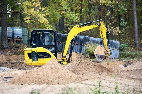 Mini excavator at construction site surrounded by trees. Compact construction Stock Photos