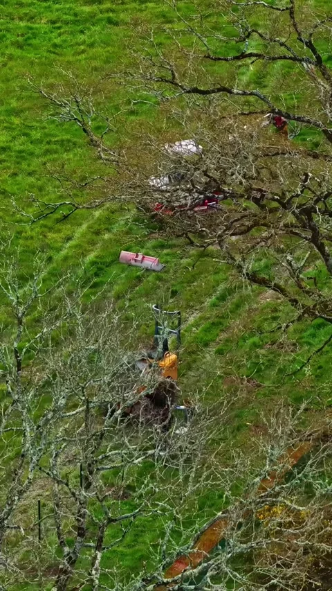 Mini excavator digging earth in a green field, aerial orbit vertical Stock Footage 335898302