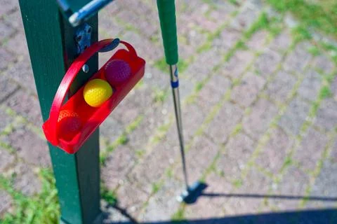 Mini golf ball holder with three balls on green post beside putter club. Stock Photos