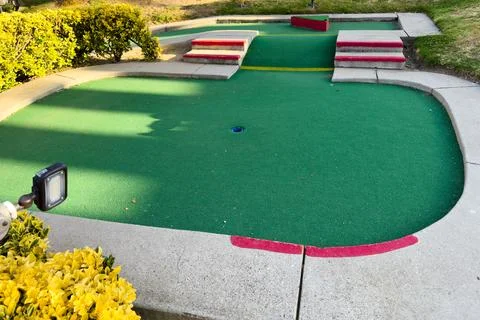 Mini-golf course with multiple holes and obstacles surrounded by greenery. Stock Photos