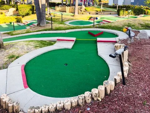 Mini-golf course with multiple holes and obstacles surrounded by greenery. Stock Photos