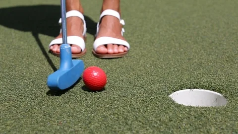 Mini golf, miniature golf or Mini Putt - woman putting with club ball in hole Stock Footage 119133398
