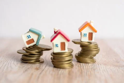 Mini house model and stack of coins. House on a coin that is about to fall. Foto stock