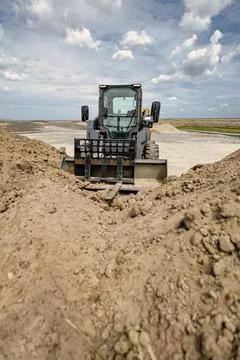 A mini loader is at work on a landscaping project, moving dirt and shaping .. Stock Photos
