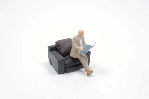A mini Man sitting on sofa reading book Stock Photos