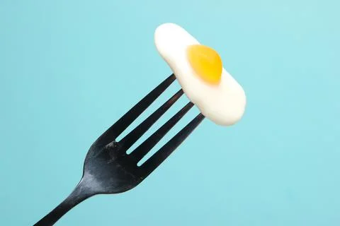 Mini marmalade fried eggs on a fork. Blue pastel background. Stock Photos