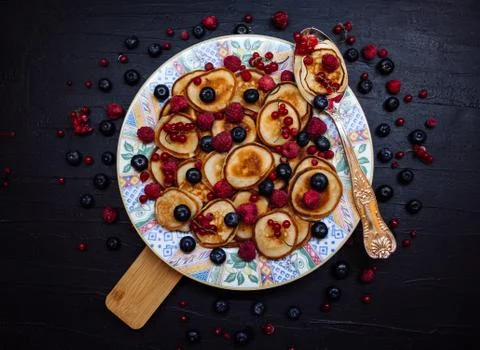 Mini pancakes with berries on a patterned plate with silver spoon in rustic s Stock Photos