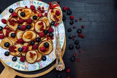 Mini pancakes with berries on a patterned plate with silver spoon in rustic s Stock Photos